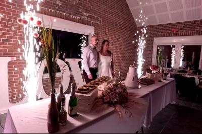 Un couple debout devant une table décorée avec des desserts, un bouquet et des fontaines lumineuses allumées.