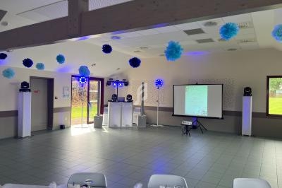 Salle décorée pour un événement avec des tables dressées, des pompons suspendus et un écran de projection installé.