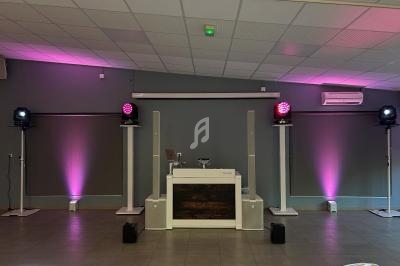 Installation de matériel de sonorisation et éclairage avec lumières roses dans une salle au plafond en dalles blanches.