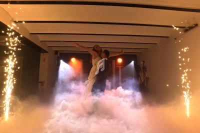 Un couple danse au milieu d'une scène enveloppée de fumée, entourée d'étincelles et éclairée par des projecteurs.