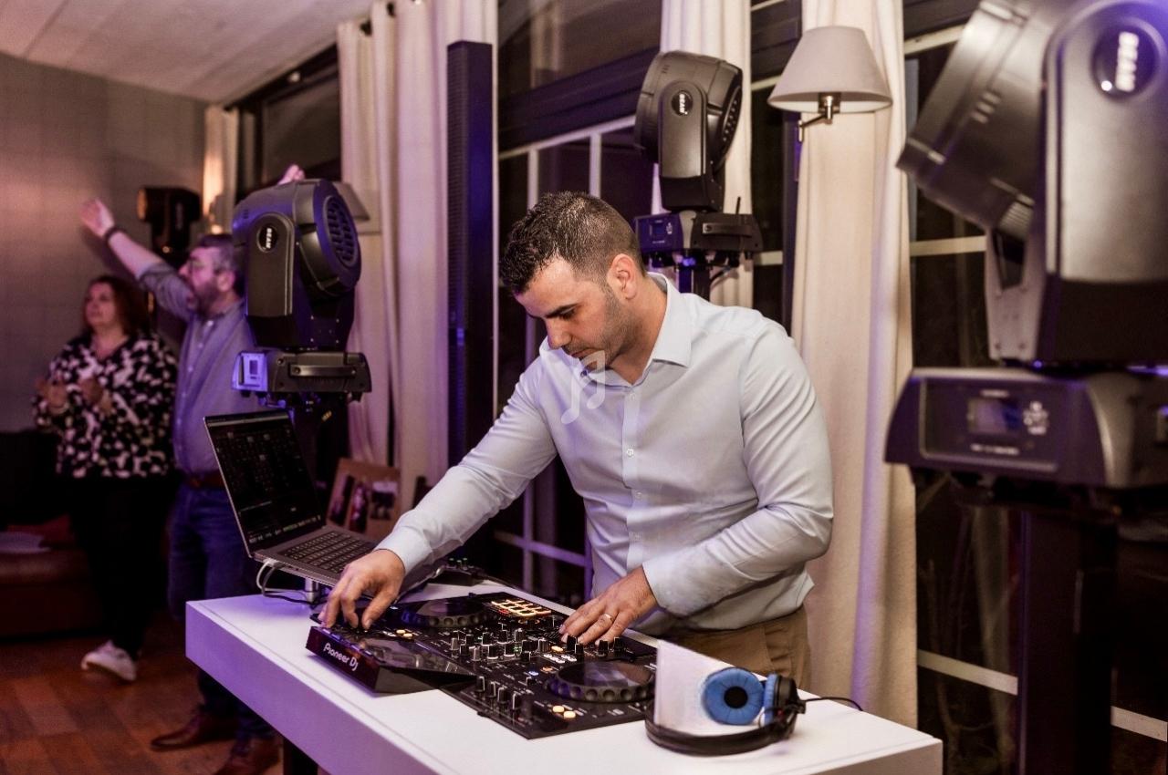 Un DJ mixe de la musique sur une table de mixage dans une salle équipée de projecteurs et de rideaux clairs.