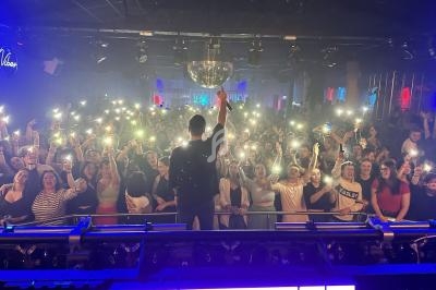 Un chanteur sur scène face à une foule brandissant des téléphones allumés dans une salle de concert.
