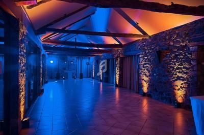 Salle en pierres apparentes avec poutres en bois, éclairée par des lumières colorées bleues et orange.