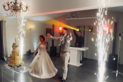 Un couple de mariés danse sous des étincelles près d'un gâteau de mariage dans une salle éclairée.