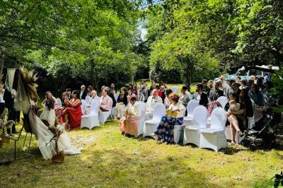 Cérémonie en plein air avec des invités assis sur des chaises blanches, entourés de verdure et de décorations naturelles.