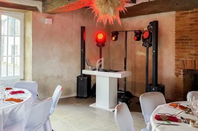 Installation d'un espace DJ avec éclairage rouge dans une salle de réception décorée, tables dressées autour.