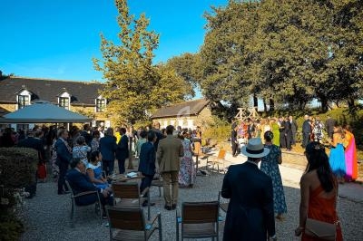 Groupe de personnes rassemblées en extérieur lors d'un événement, près de bâtiments en pierre et d'arbres sous un ciel…