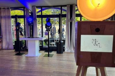 Cabine photo en bois devant une piste de danse équipée de lumières et d'une table de DJ, dans une salle lumineuse.