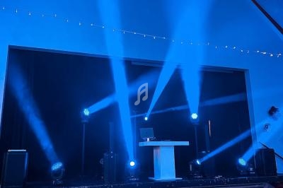 Scène éclairée par des projecteurs bleus avec une table blanche et un ordinateur portable au centre.