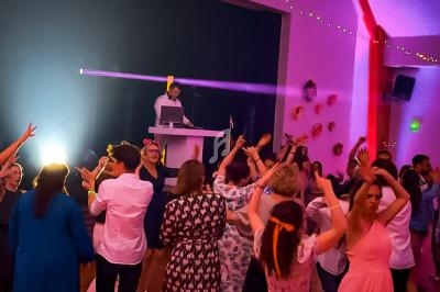 Personnes dansant lors d'une soirée festive avec un DJ sur scène et des lumières colorées en arrière-plan.