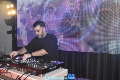 Un DJ mixe sur une table de mixage devant un écran lumineux affichant des motifs colorés.