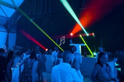 Des personnes dansent sous des jeux de lumières colorées dans une salle sombre avec une scène équipée d'un pupitre.