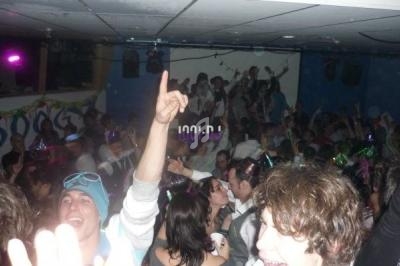 Foule de personnes dans une soirée festive en intérieur, dansant et célébrant sous des lumières colorées.