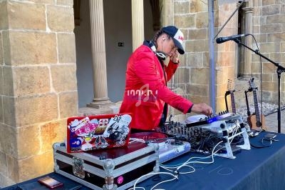 Un DJ mixant de la musique sur une table équipée de matériel audio, dans un cadre architectural en pierre.
