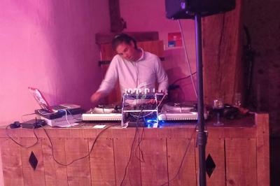 Un DJ mixe de la musique derrière une table en bois, entouré d'équipements audio dans une pièce à l'éclairage tamisé.