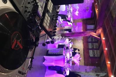 Vue d'une salle de réception décorée avec des tables dressées et éclairage violet, avec une platine DJ au premier plan.