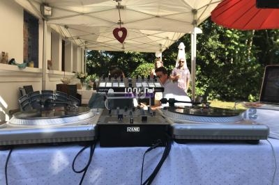 Deux platines et une table de mixage sous une tente blanche, avec des personnes en arrière-plan.
