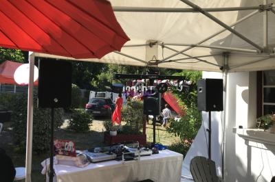 Matériel de sonorisation et de mixage installé sous une tente lors d'un événement en extérieur, avec des invités en arrière…