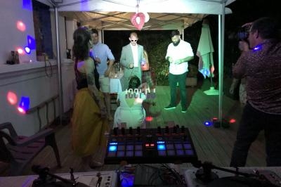 Personnes dansant et discutant sous une tente éclairée, avec une table de mixage au premier plan.