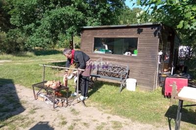 Un homme cuisine des morceaux de viande sur un barbecue en plein air, près d'une cabane en bois.