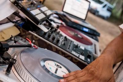 Un DJ manipule un vinyle sur une platine lors d'un événement en plein air, avec des équipements audio visibles.