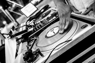 Un DJ manipule un disque vinyle sur une platine, avec un ordinateur et une table de mixage en arrière-plan.