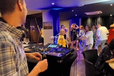 Un DJ anime une soirée dansante dans une salle éclairée, avec des invités qui dansent en arrière-plan.