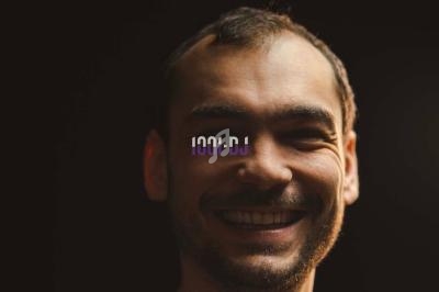 Portrait d'un homme souriant avec un éclairage tamisé et un logo ’1001 DJ’ superposé sur son visage.