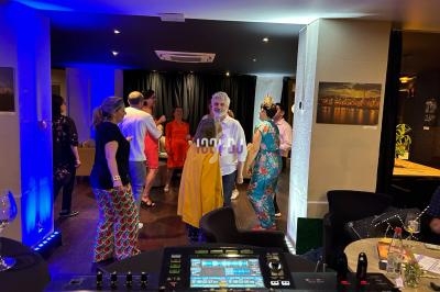 Des personnes dansent dans une salle éclairée avec un DJ en arrière-plan et des tables dressées sur les côtés.