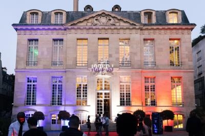 Façade d'un bâtiment historique éclairée de lumières colorées, avec des personnes rassemblées devant l'entrée.