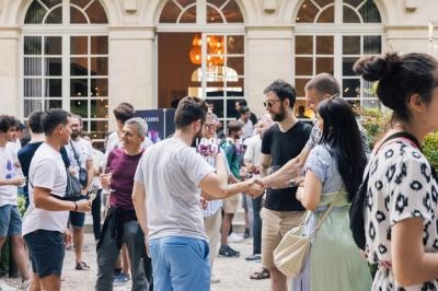 Un groupe de personnes échange et discute dans une cour extérieure devant un bâtiment avec de grandes fenêtres.