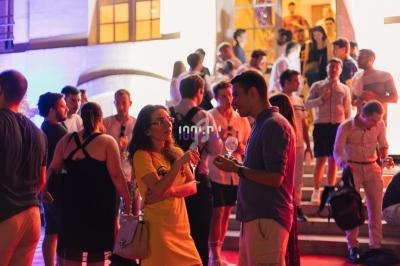 Groupe de personnes discutant et socialisant lors d'un événement en soirée devant un bâtiment éclairé.