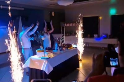Un couple danse devant une table décorée avec des gâteaux, entouré de fontaines lumineuses dans une salle sombre.