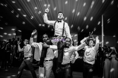 Un homme en tenue de soirée est porté par quatre autres hommes dans une salle de réception éclairée par des spots.