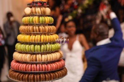 Tour de macarons colorés sur un présentoir, avec des invités flous en arrière-plan lors d'un événement festif.