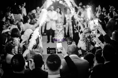 Des mariés avancent sous des étincelles tenues par des invités, entourés d'une foule capturant le moment avec leurs…