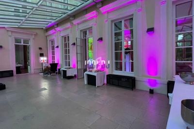 Salle lumineuse avec verrière, murs clairs, éclairage rose et mobilier disposé pour un événement.