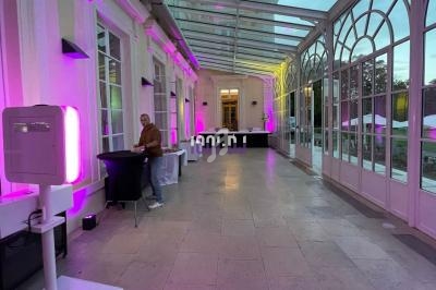 Intérieur d'une verrière éclairée par des lumières roses, avec une personne près d'une table haute.