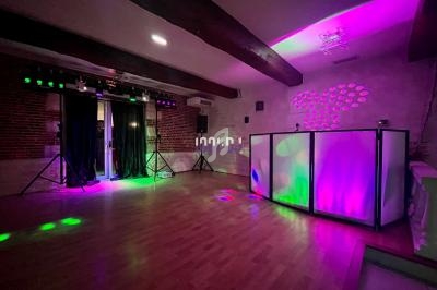 Salle avec parquet, éclairages colorés, rideaux noirs, murs en briques et espace DJ équipé de lumières LED.