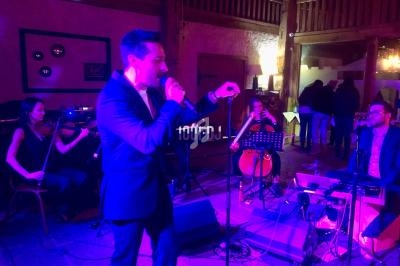 Un chanteur se produit sur scène accompagné de musiciens jouant du violon, du violoncelle et du clavier dans une salle…