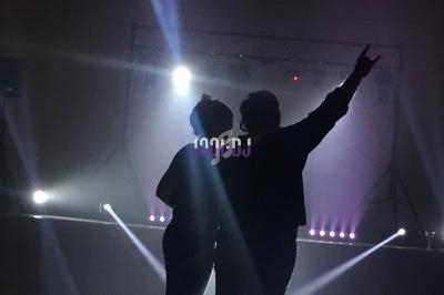 Deux personnes de dos dans une salle sombre, éclairées par des projecteurs et des lumières de scène.