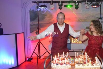 Un homme et une femme en tenue de soirée soufflent des bougies sur des gâteaux lors d'une fête dans une salle éclairée.