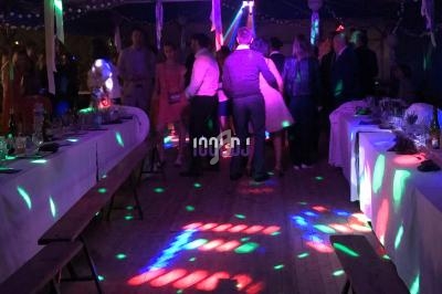 Personnes dansant sous des lumières colorées dans une salle décorée avec des tables alignées.