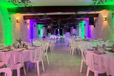 Salle de réception décorée avec des tables rondes dressées, éclairage coloré et guirlandes végétales suspendues.