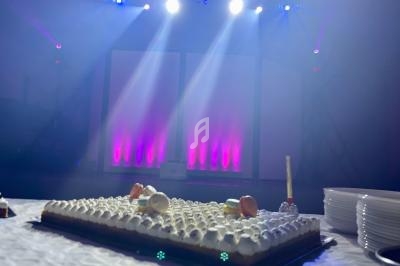 Gâteau décoré avec des macarons sur une table, éclairé par des projecteurs colorés dans une salle sombre.