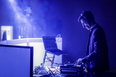 Un DJ mixant de la musique sur une table de mixage, éclairé par des lumières bleues dans une ambiance sombre.