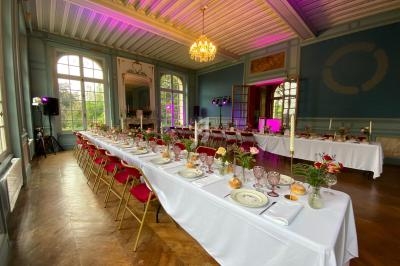 Salle de réception élégante avec tables dressées, chaises rouges et lumière tamisée sous un lustre central.