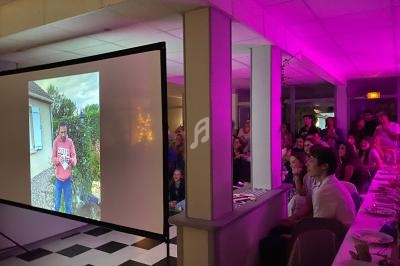Projection d'une photo sur un écran dans une salle éclairée par des lumières roses, avec des invités attentifs.
