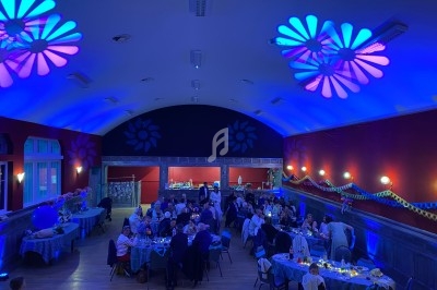 Salle de réception décorée, éclairée en bleu, avec des invités assis à des tables pour un événement festif.