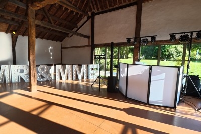 Salle de réception lumineuse avec des lettres lumineuses ’MR & MME’ et un espace DJ équipé.